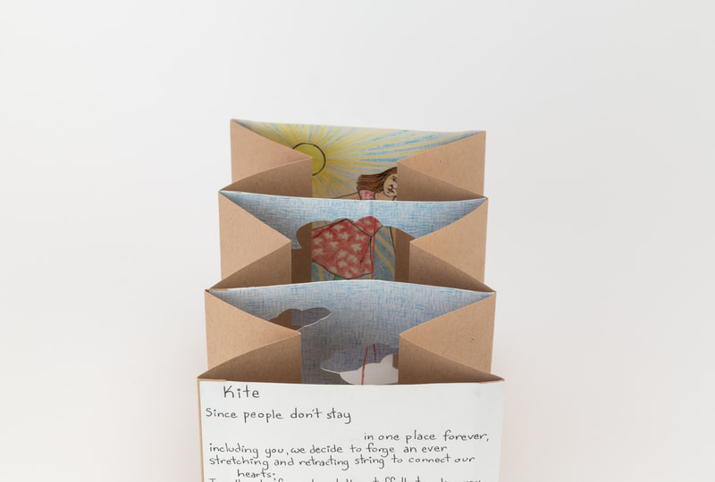 Accordion art book with four panels viewed from above. The front panel has the beginning of a poem titled "Kite" written on it. The middle two panels have cloud shapes cut out of them. The last panel has an illustration of a young person in a dress floating in front of a sun.